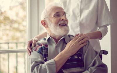 Senior man sitting on the wheelchair, laughing and holding his nurse's hand